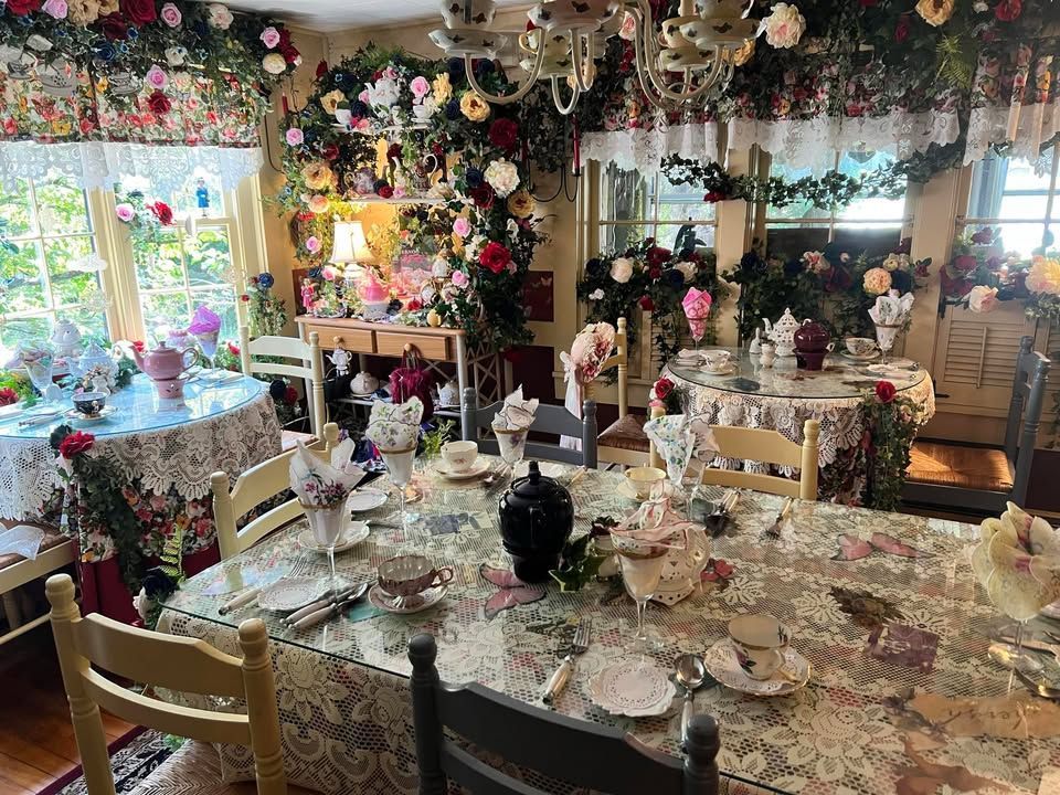 A lavish dining room decorated with roses, floral arrangements, and lace tablecloths, set for a tea party. A lavish dining room decorated with roses, floral arrangements, and lace tablecloths, set for a tea party.