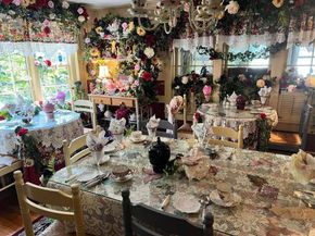 A lavish dining room decorated with roses, floral arrangements, and lace tablecloths, set for a tea party.