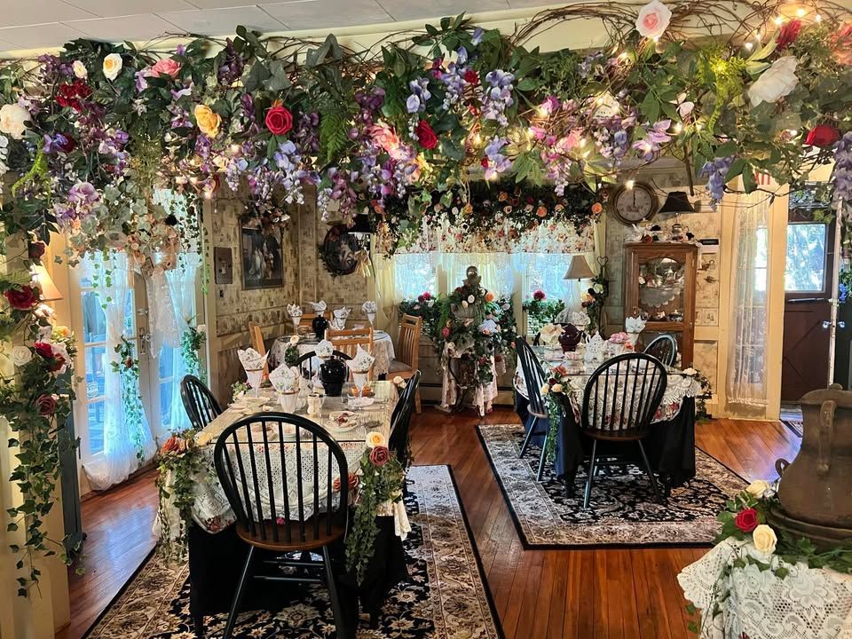 A dining room lavishly decorated with flowers and greenery. Tables are set with elegant place settings, ready for a tea party or meal.