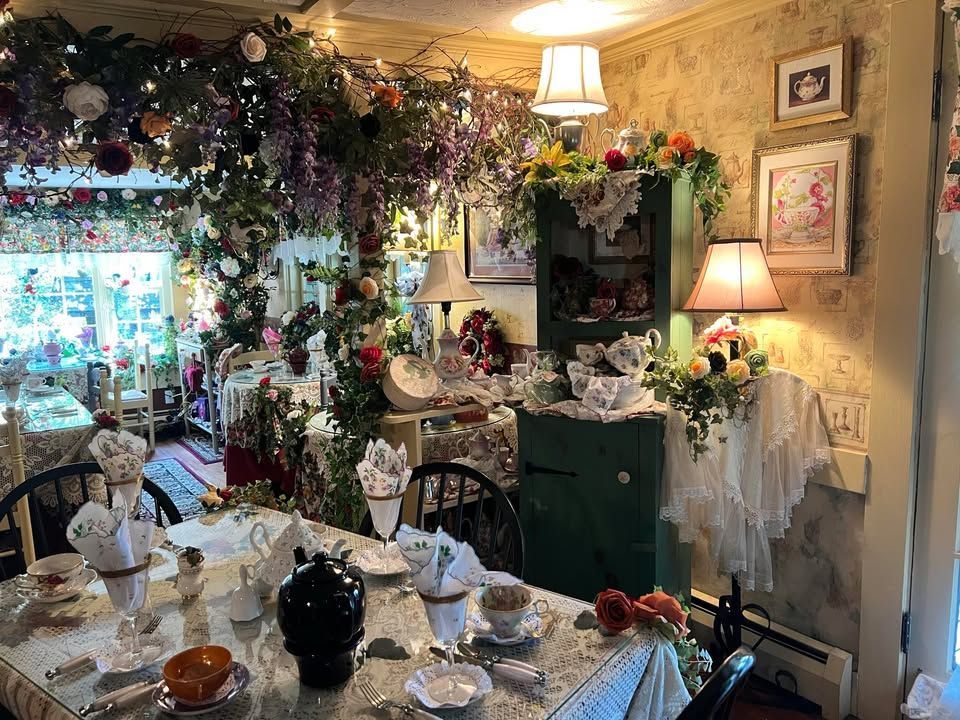 Tea room interior, tables set with china, floral decorations, small green cabinet, lamps, and wisteria vines.