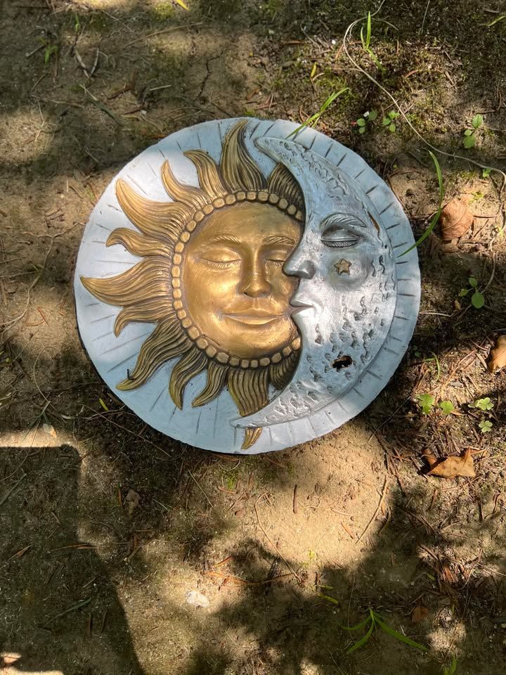 Sun and moon garden ornament with gold sun and silver moon face. It is on a brick path.