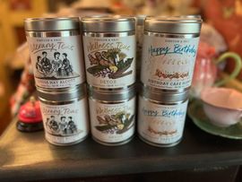 Six silver-lidded tea tins stacked in two rows. Each tin features a different label. Six silver-lidded tea tins stacked in two rows. Each tin features a different label.