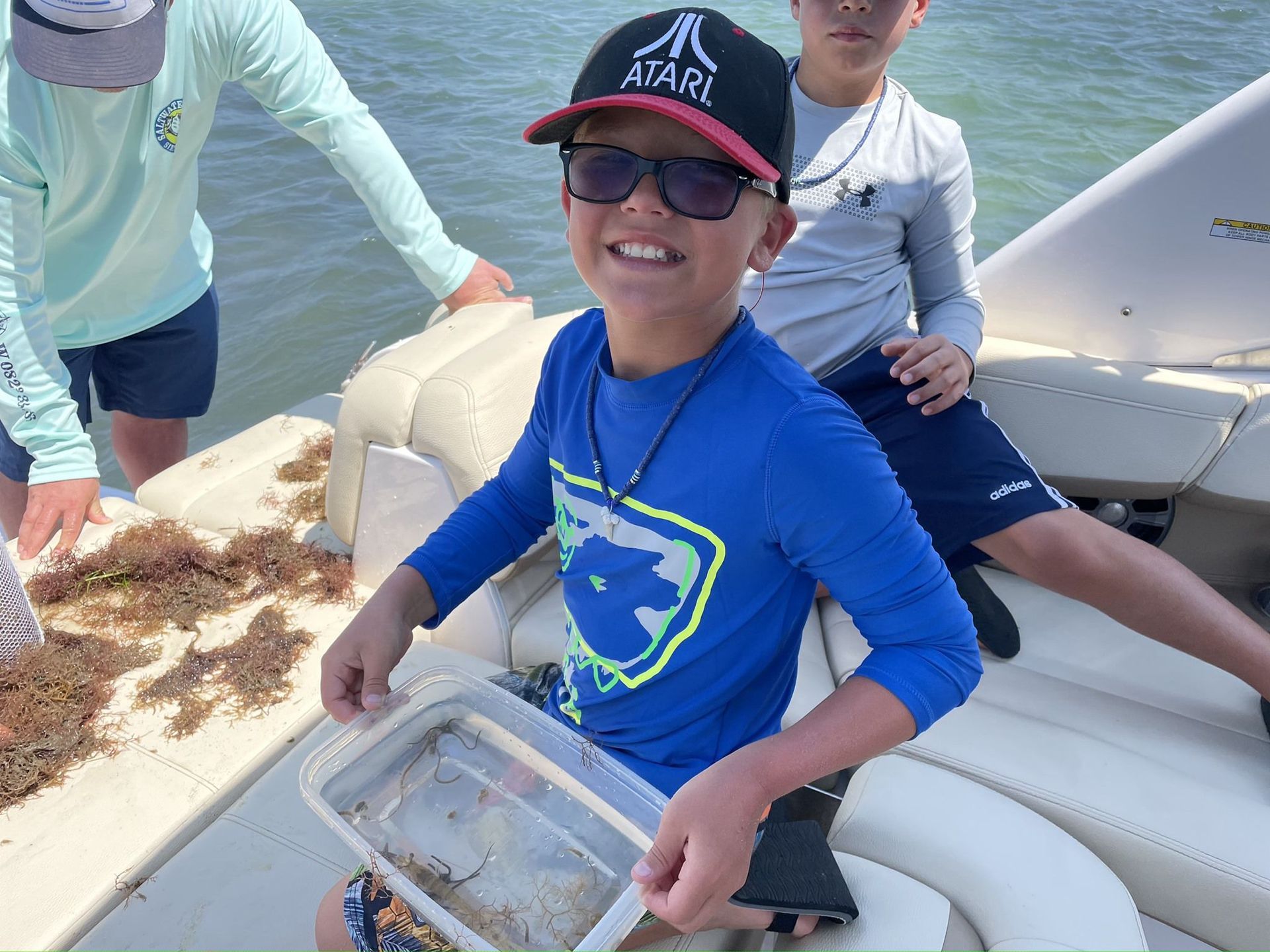 A boy wearing a hat and sunglasses is sitting on a boat.