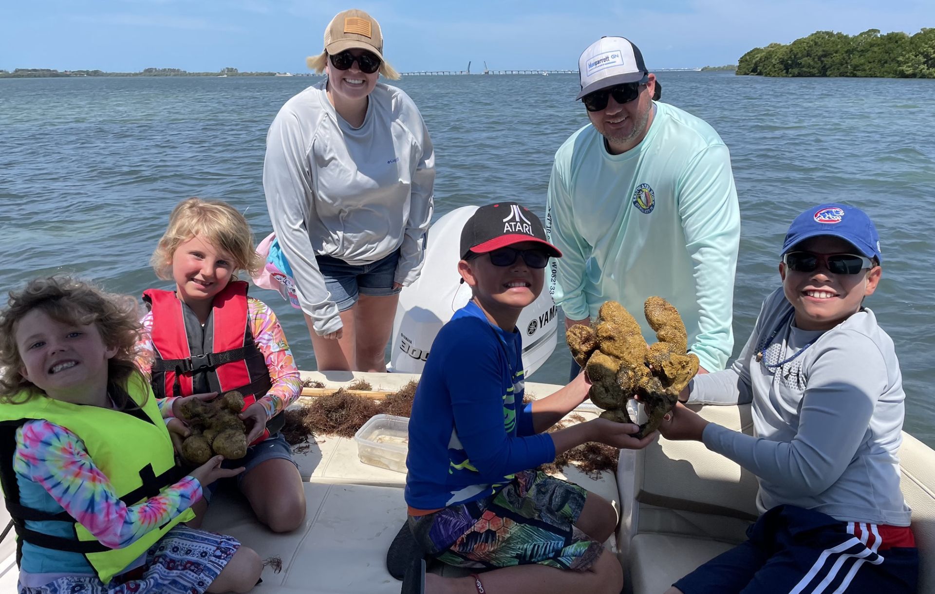 A group of people are sitting on a boat in the water holding coral.