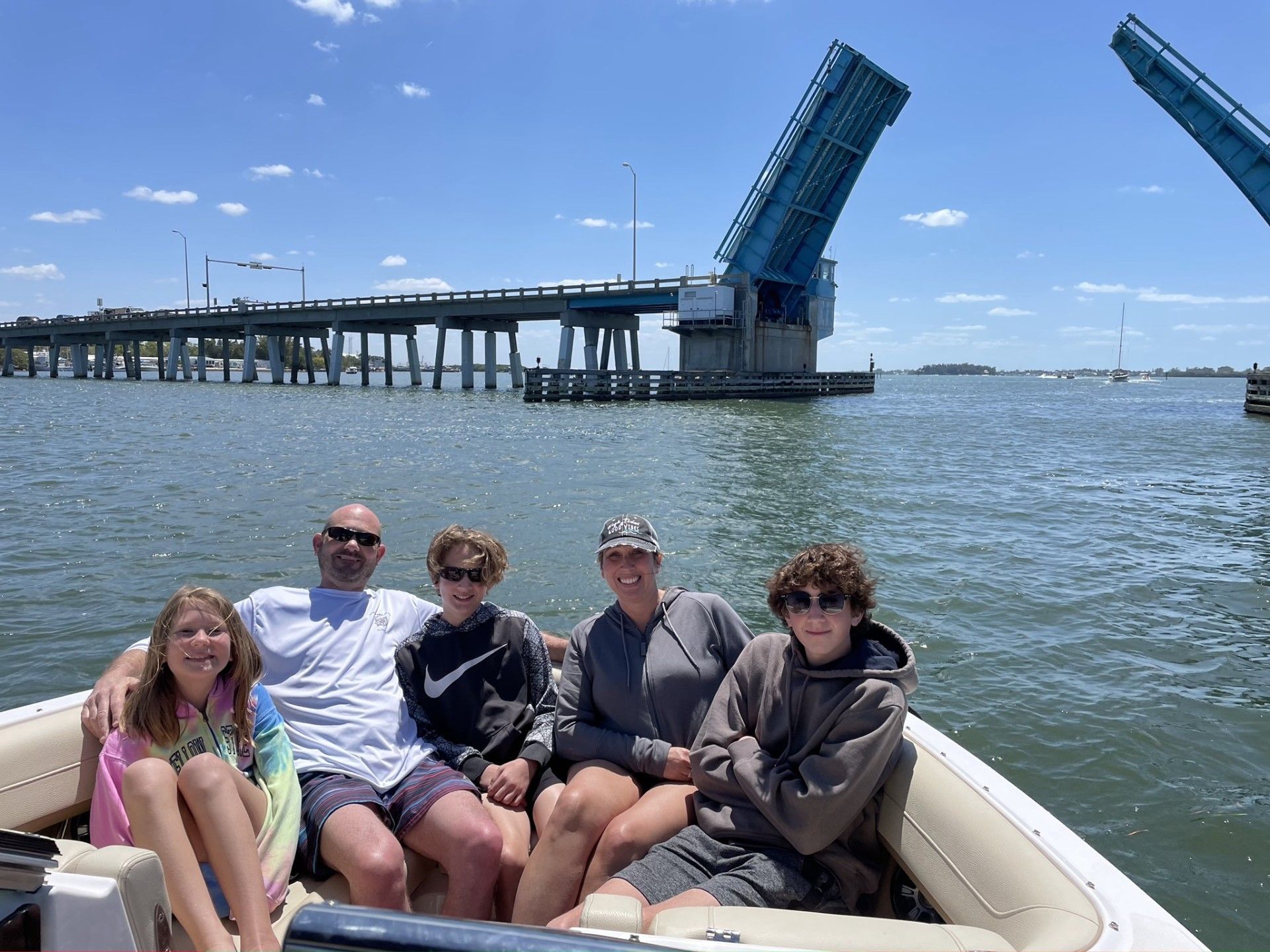 A family is sitting on a boat in the water with a bridge in the background.