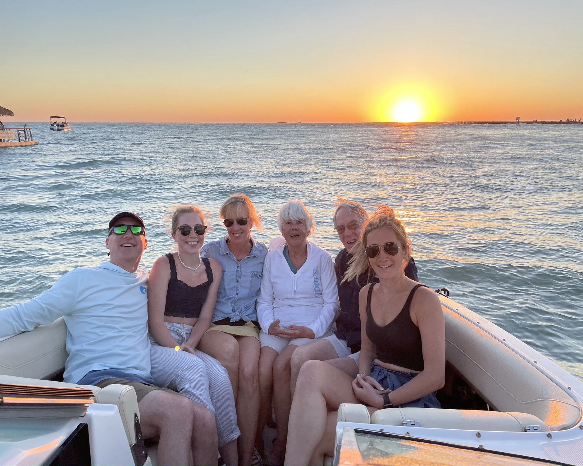 Happy family are sitting on a boat in the ocean at sunset.