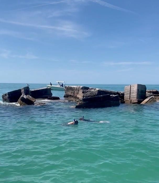 People snorkeling in aqua waters near ruins