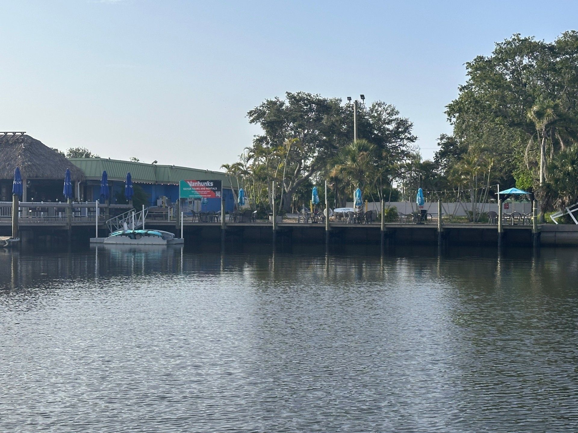 Water view of a dock with a boat and a waterside restaurant under a clear sky.