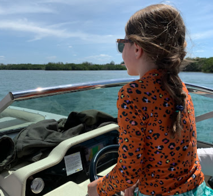 A little girl in a leopard print shirt is driving a boat