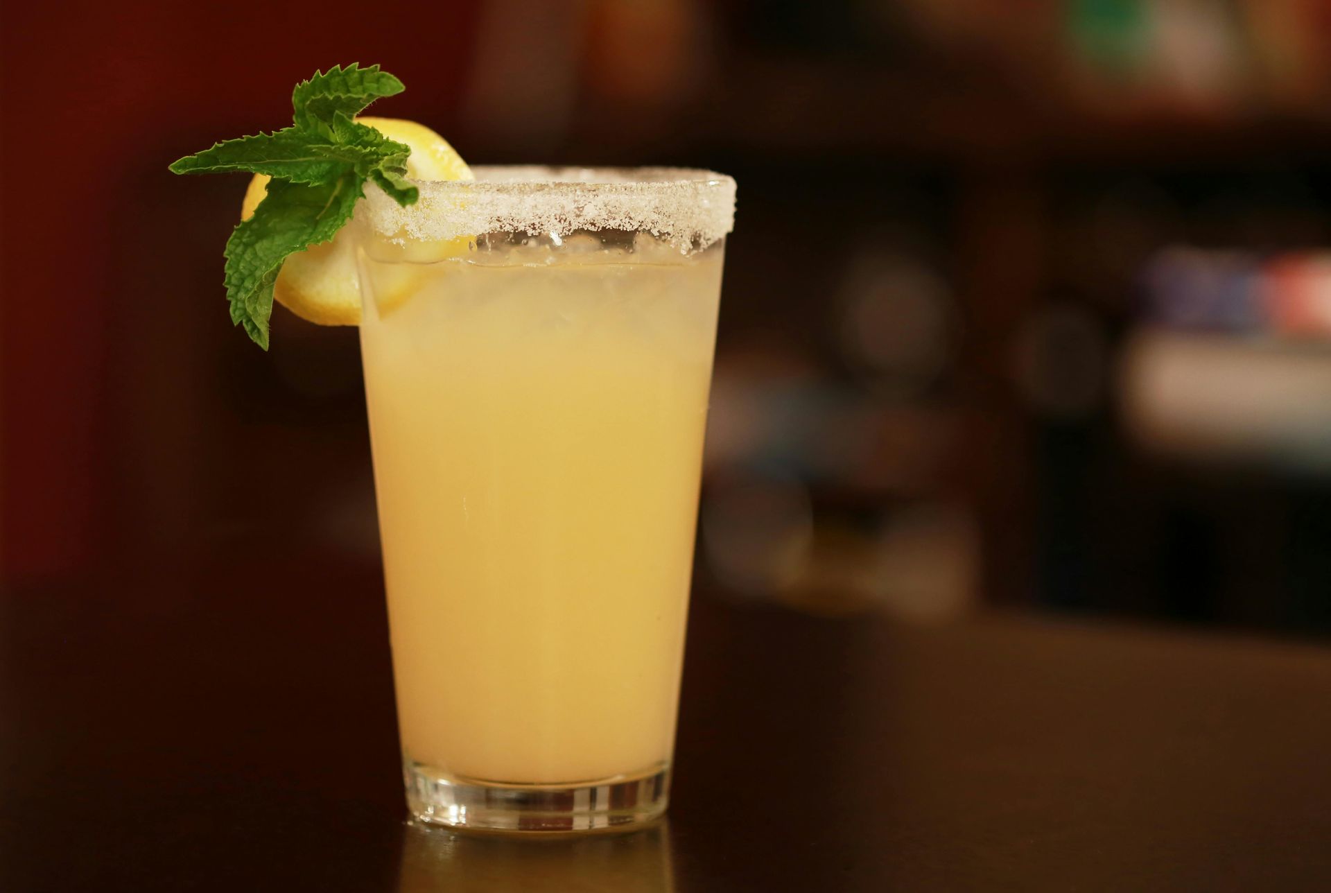 A glass of lemonade with a slice of lemon and mint on a table.