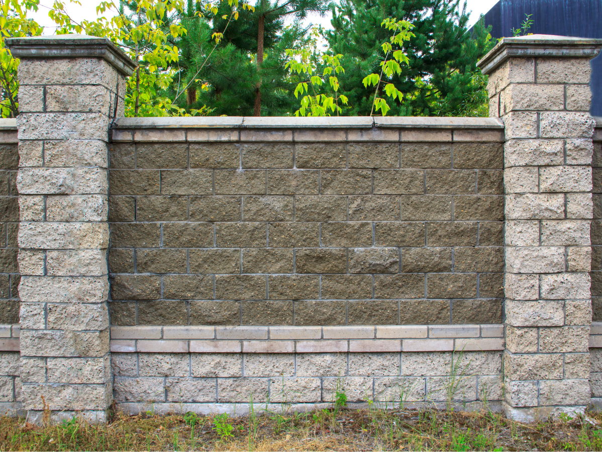 Stone fence with two pillars, trees in the background.