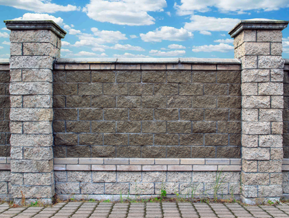 Stone fence with pillars against a blue sky with clouds.