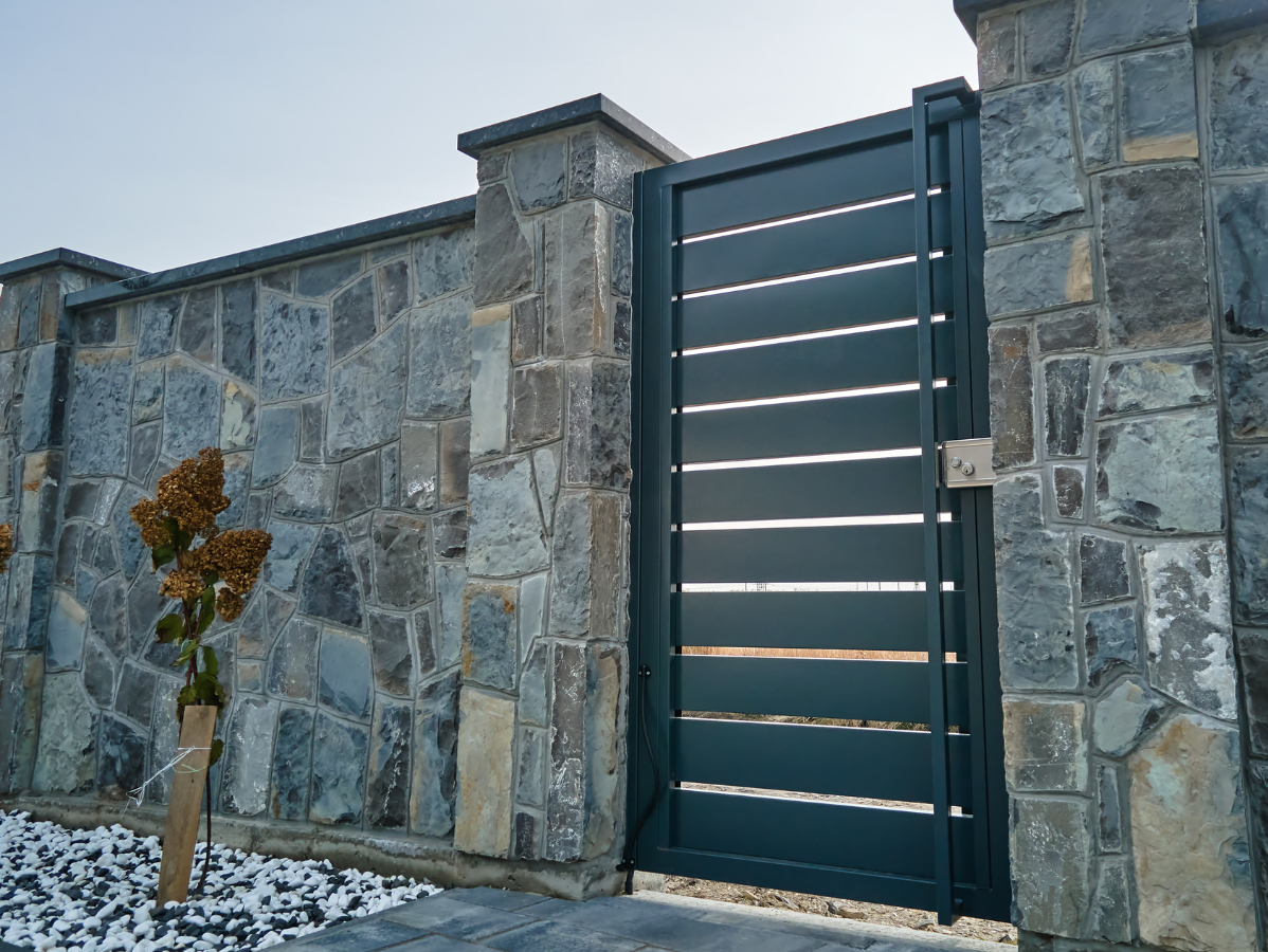 Black metal gate with horizontal slats set in a stone wall.
