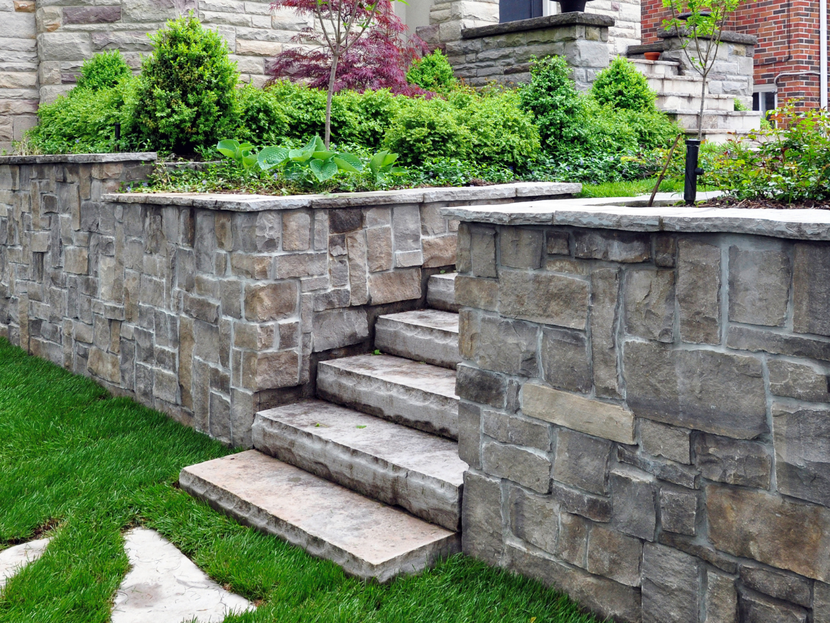 Stone steps leading up to a raised garden bed with green plants, grass lawn.
