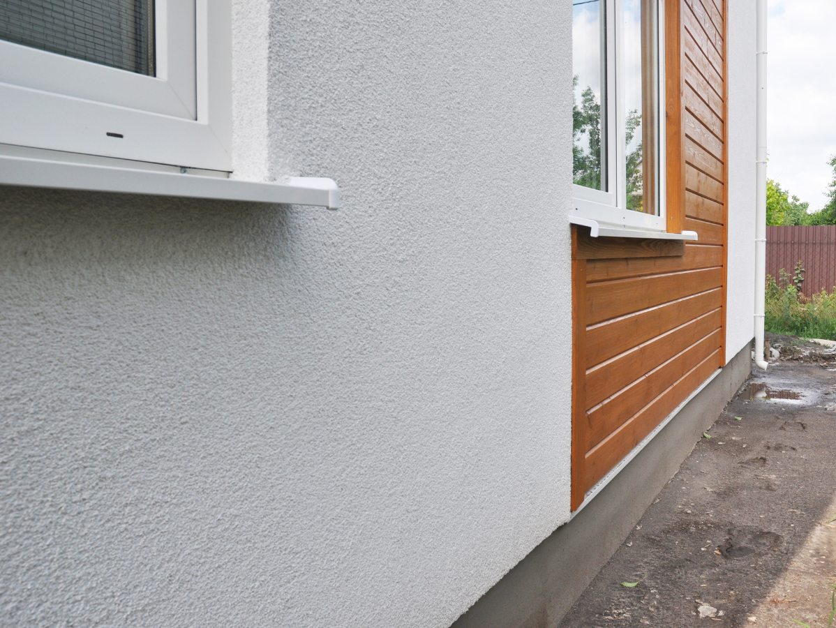 Exterior wall with white textured finish and brown wood siding near a window.