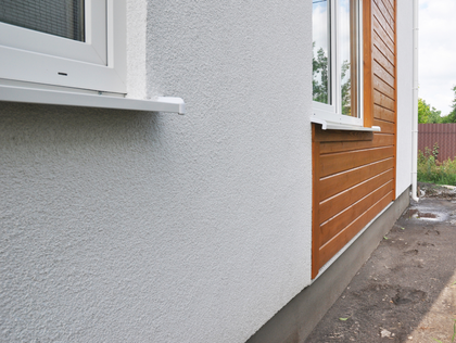 Exterior wall of a building with white textured stucco and wood paneling next to a window.