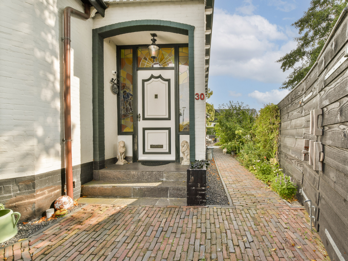White house entrance with a brick path, dark green trim, and a wooden fence.