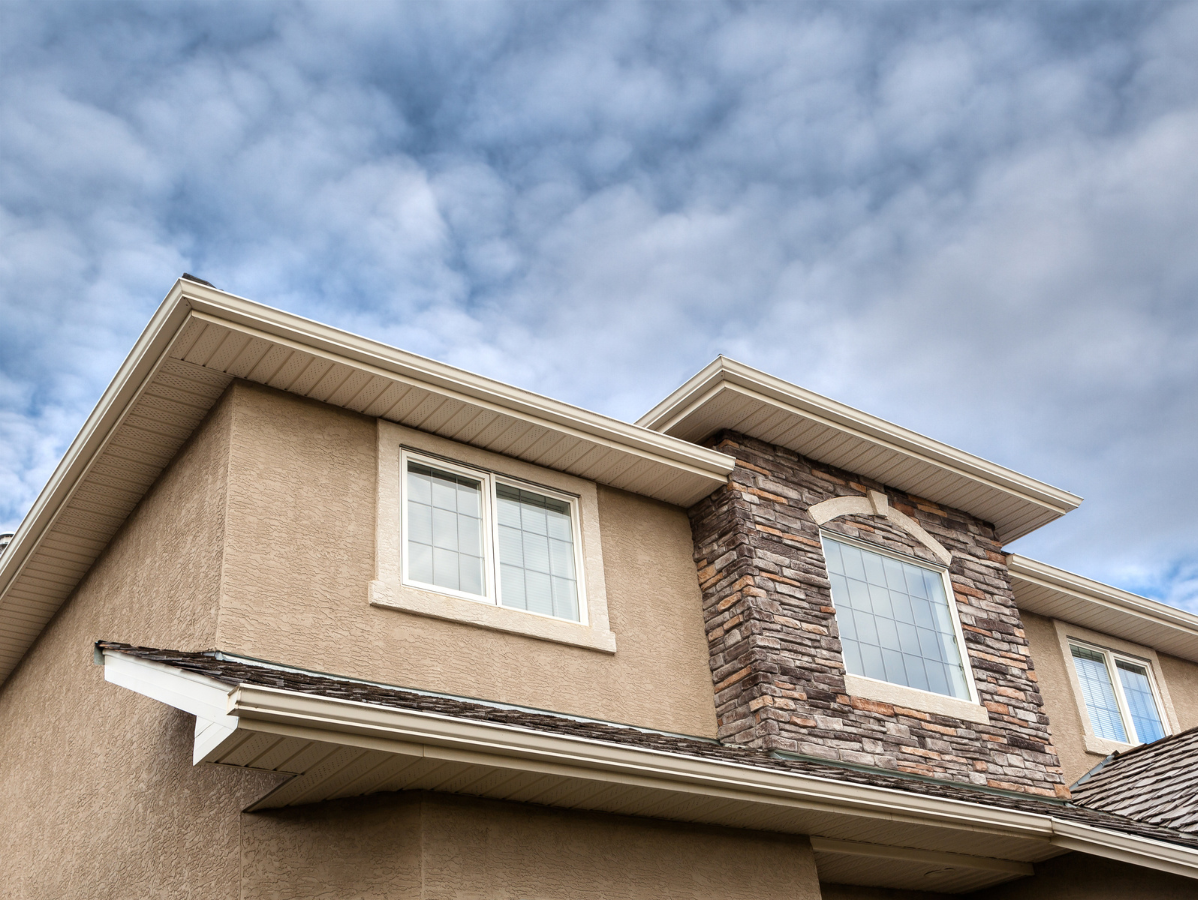 Beige stucco house with stone accents, white trim, and cloudy sky.