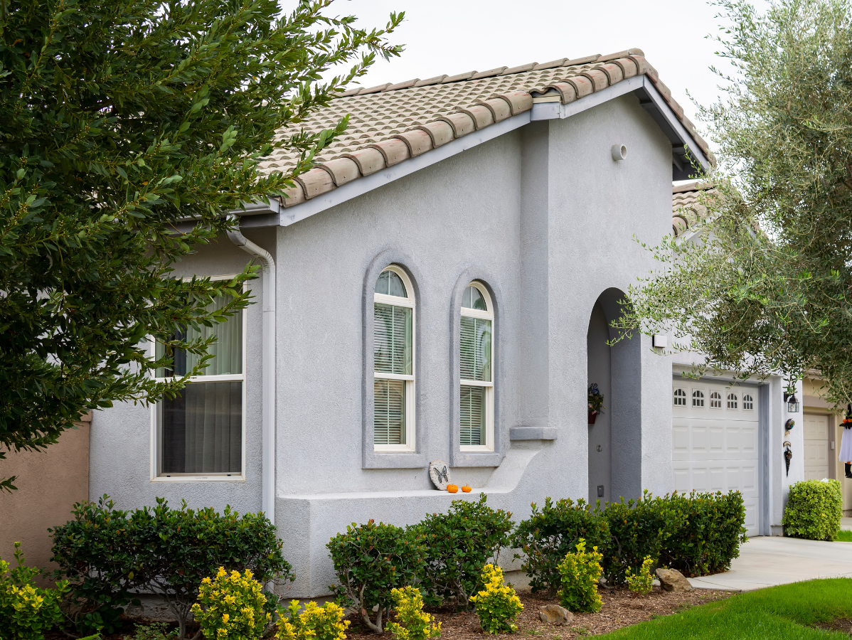 Light blue house with beige tile roof, arched windows, and green bushes.