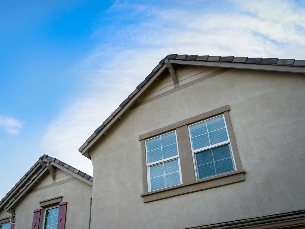 Tan houses with brown roofs against a blue sky. Windows with white frames.
