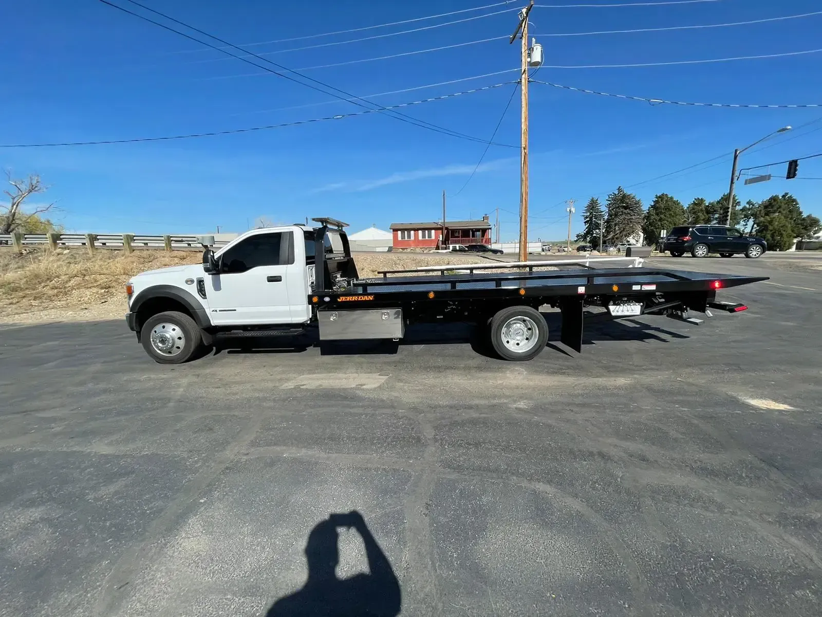White tow truck on a paved road, under a clear blue sky.