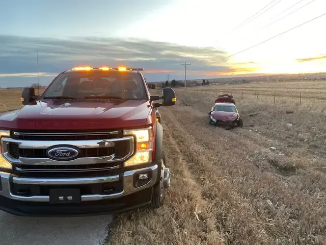 Red tow truck next to a damaged red car in a field at sunset.