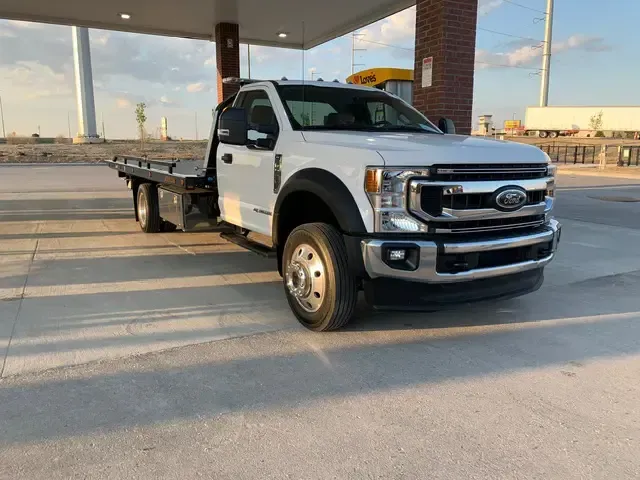 White Ford tow truck at a gas station with a flatbed.