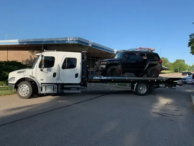 Black SUV on a white tow truck in front of a building on a paved area.