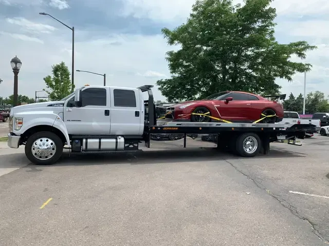 A red sports car being towed on a flatbed truck in an outdoor parking area.