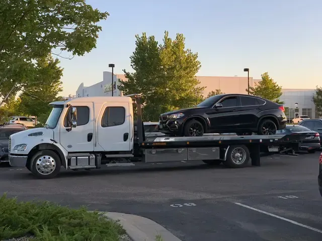 A black BMW SUV is on a white flatbed tow truck in a parking lot.