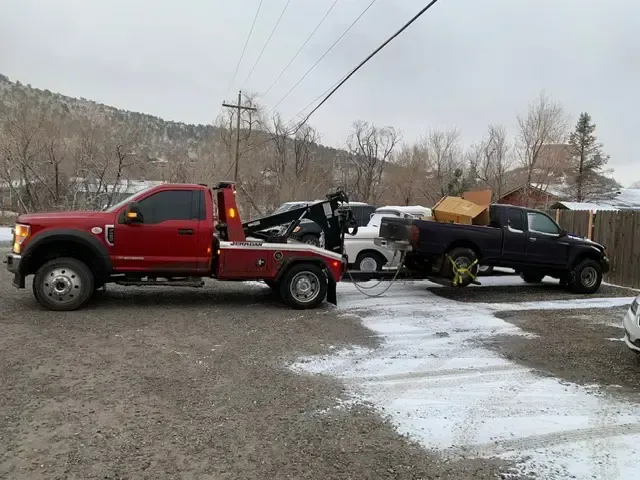Red tow truck towing a black pickup truck and a white SUV on a snowy day.