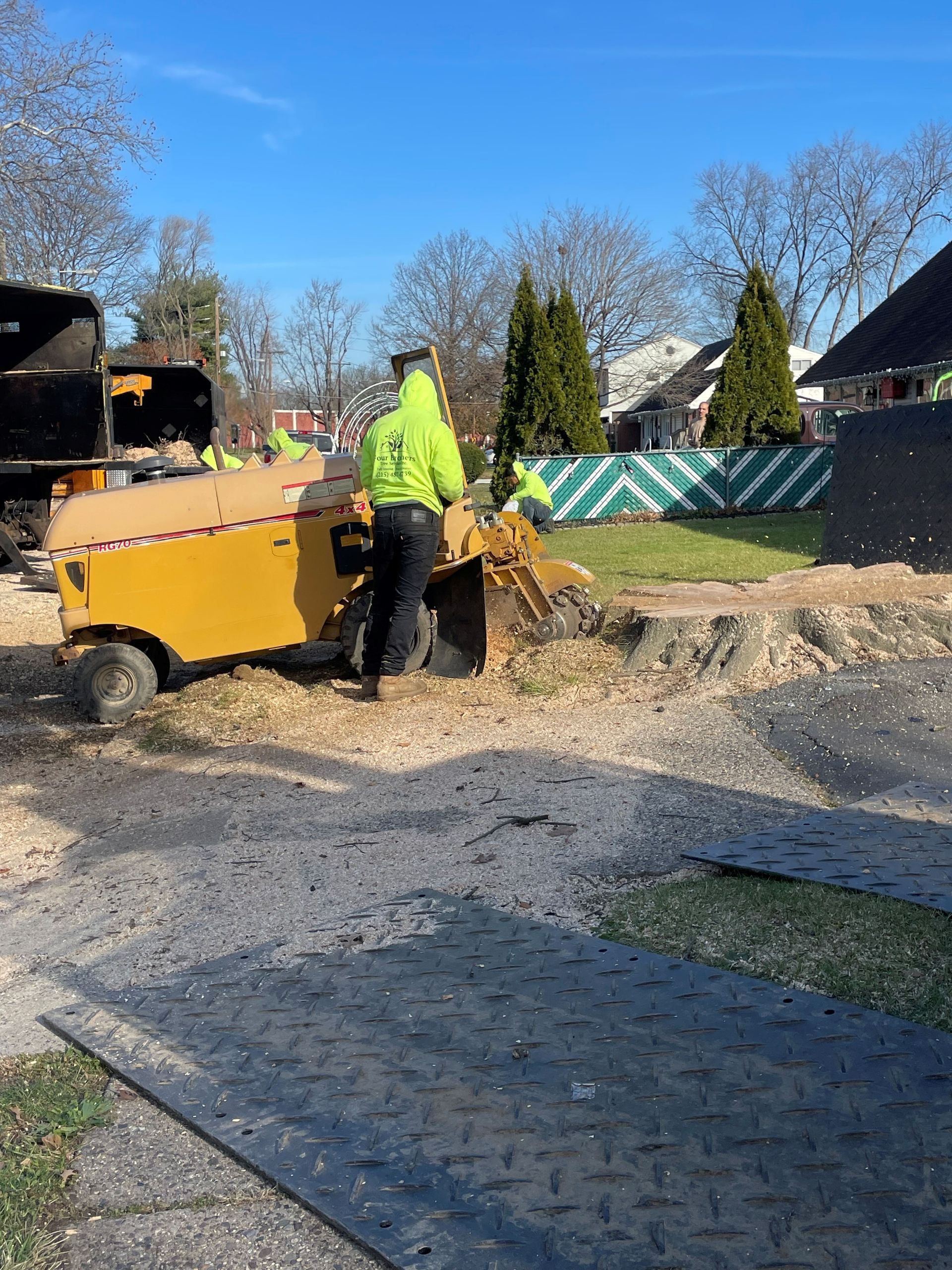 A man is standing next to a machine that is cutting a tree stump.