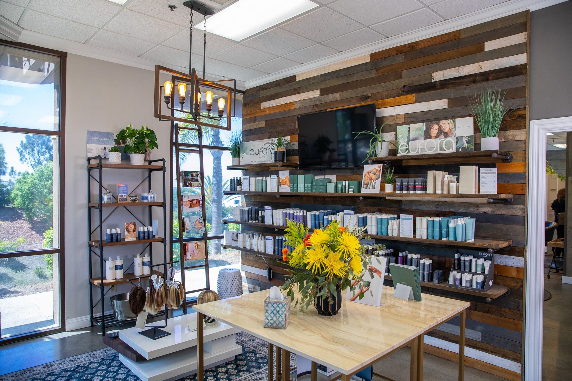 Hair and beauty salon interior with wooden wall, display shelves, products, and a table with flowers.