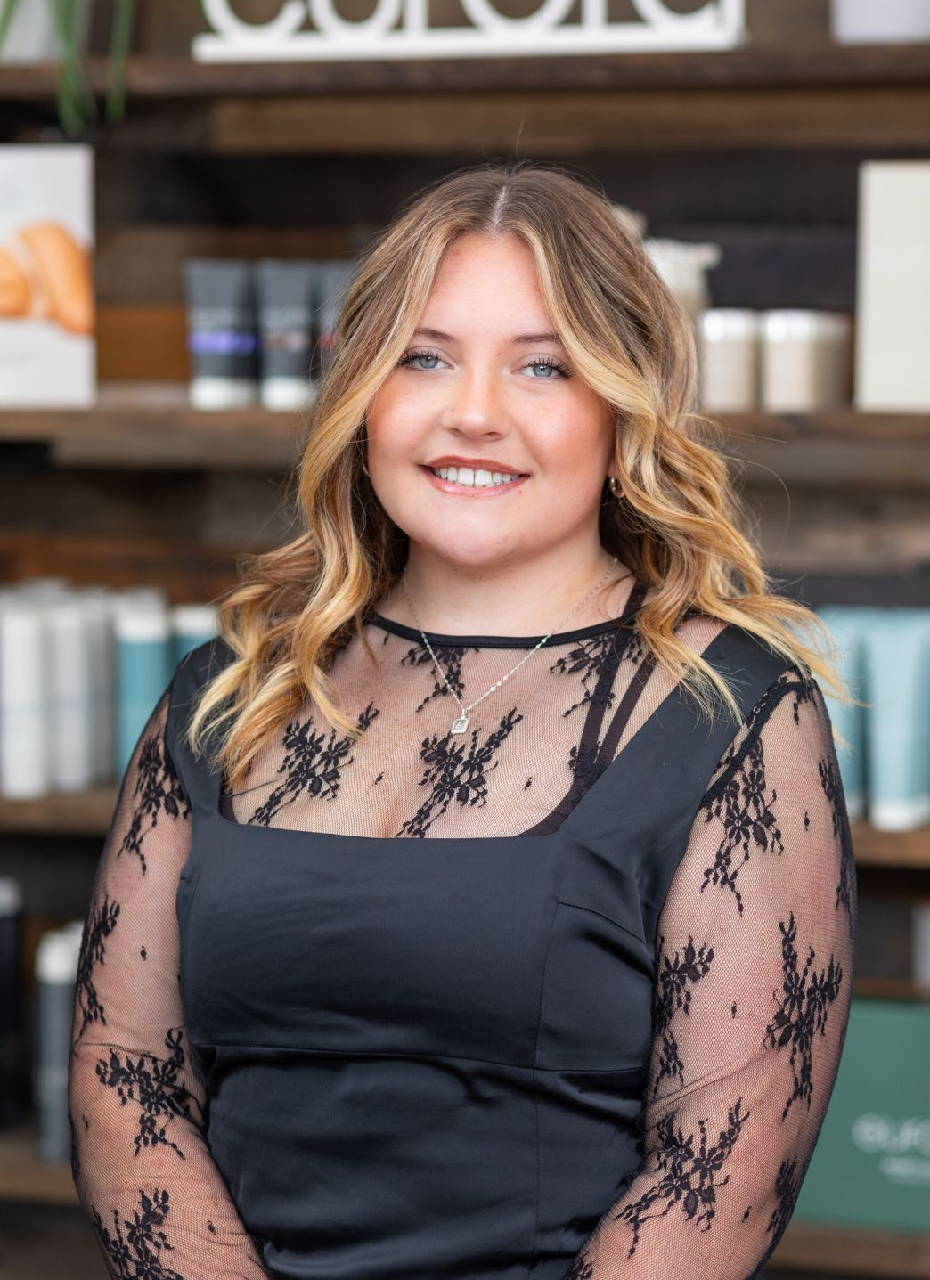Woman in black outfit smiles, arms resting on counter in beauty salon.