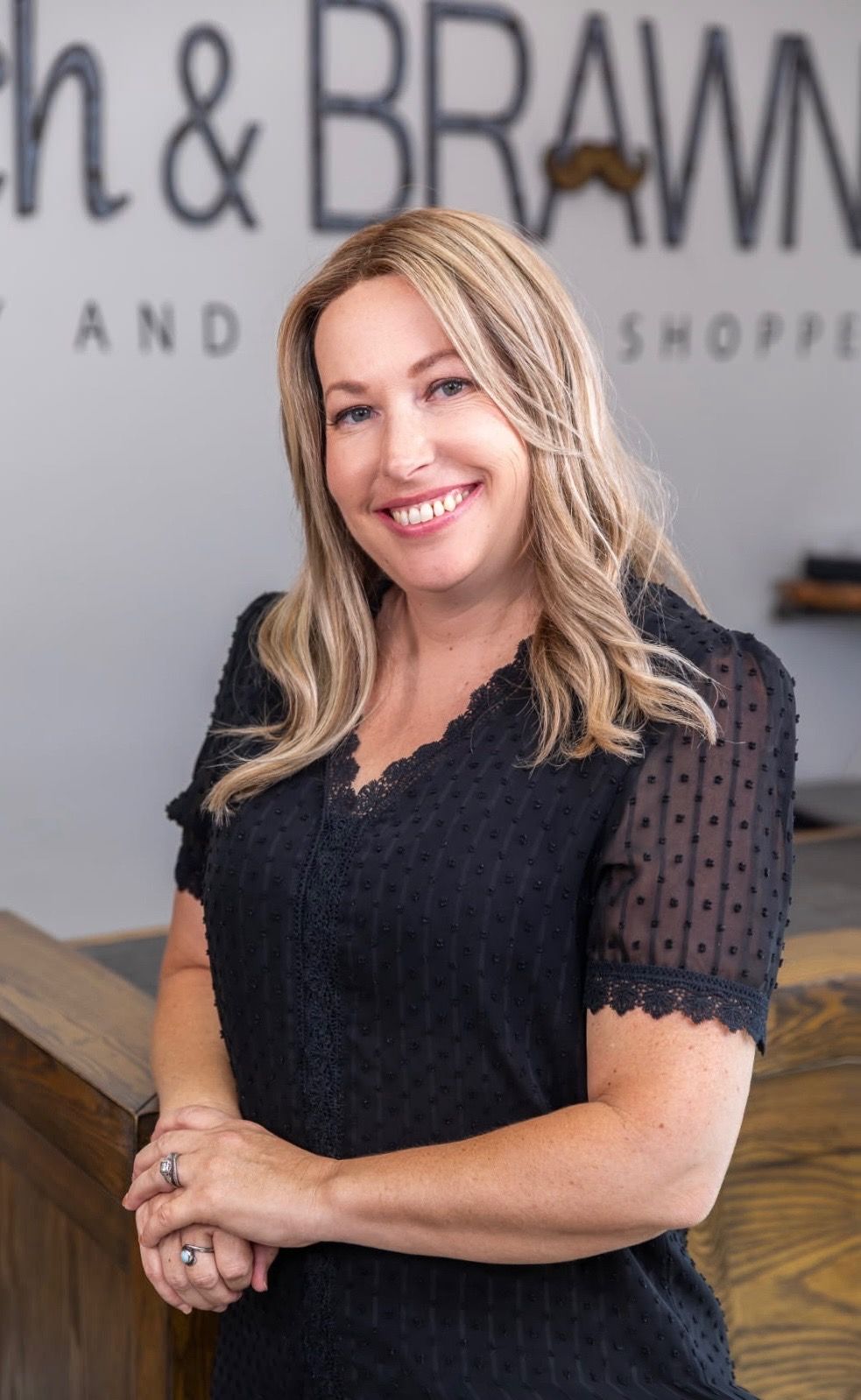 Woman in black top smiles, standing in a shop.