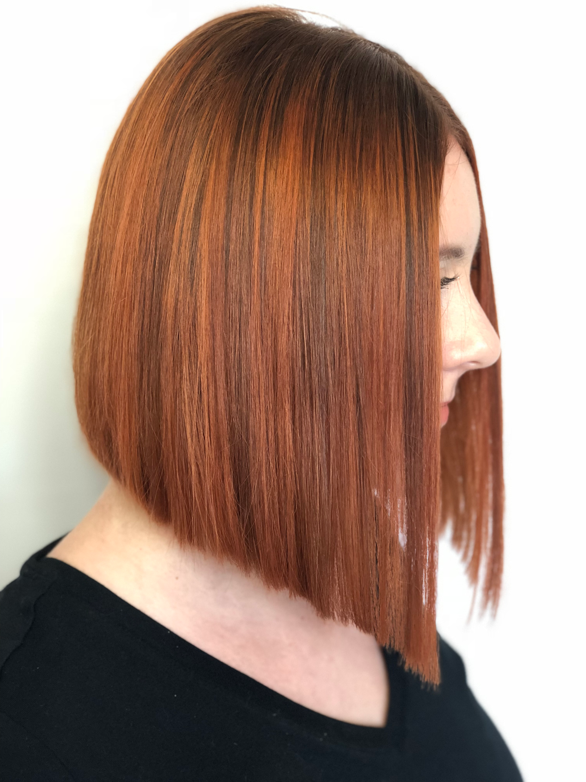 A person with a reddish-brown, angled bob haircut in front of a white background.