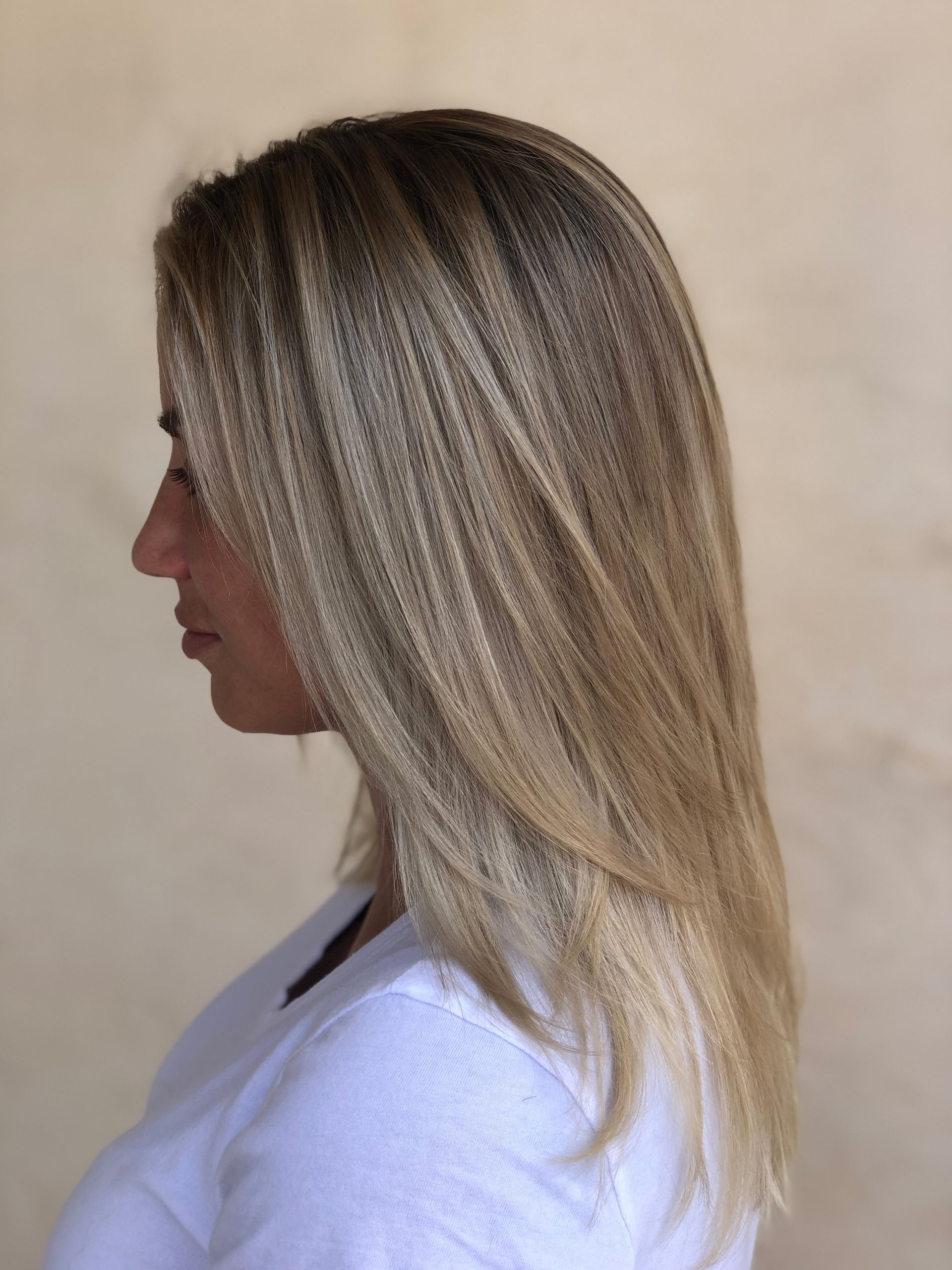 Woman in profile with long, blonde hair, wearing a white sweater, against a beige wall.