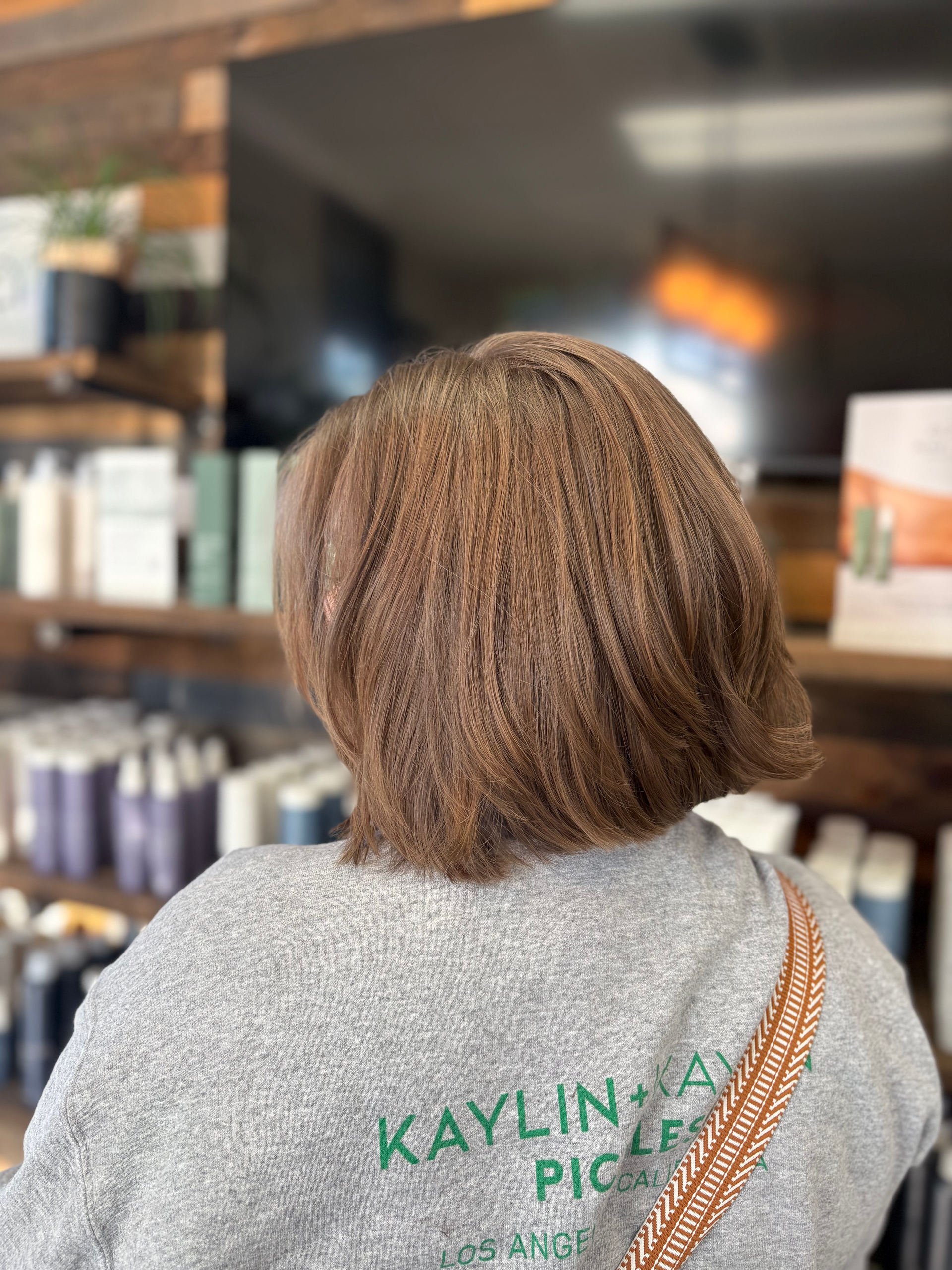 Person with brown hair, in a grey sweatshirt, at a hair salon.