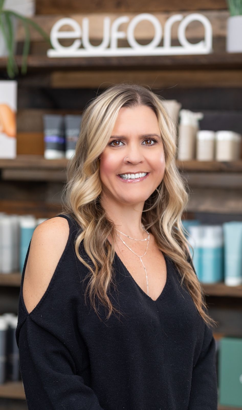 Woman with blonde hair and arm tattoo smiles at the camera in a shop.