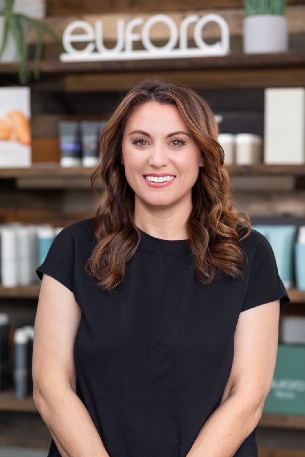 Woman in black shirt smiling, leaning on a wooden counter with a business sign in the background.