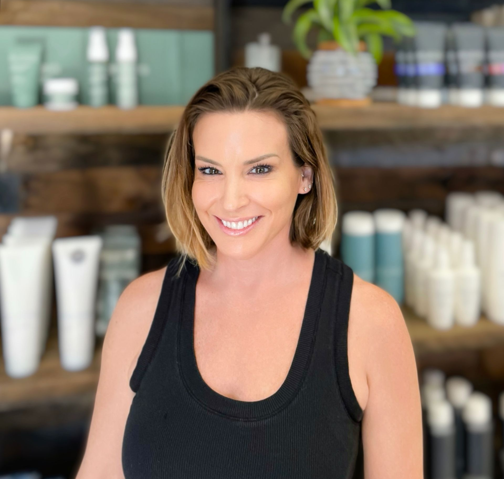 Woman in black tank top smiles in front of shelves with products.