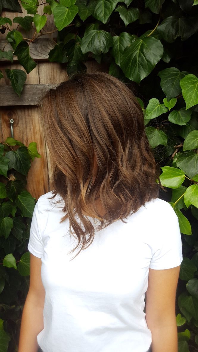 Woman with brown wavy hair wearing a white shirt, standing in front of green vines.