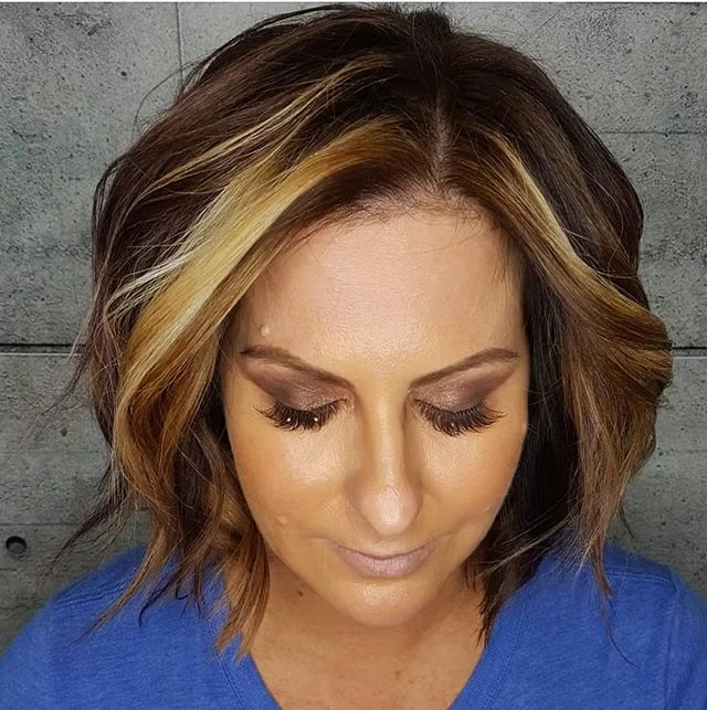 Woman with a bob hairstyle; dark brown with blonde highlights, wearing makeup and blue shirt, looking down.