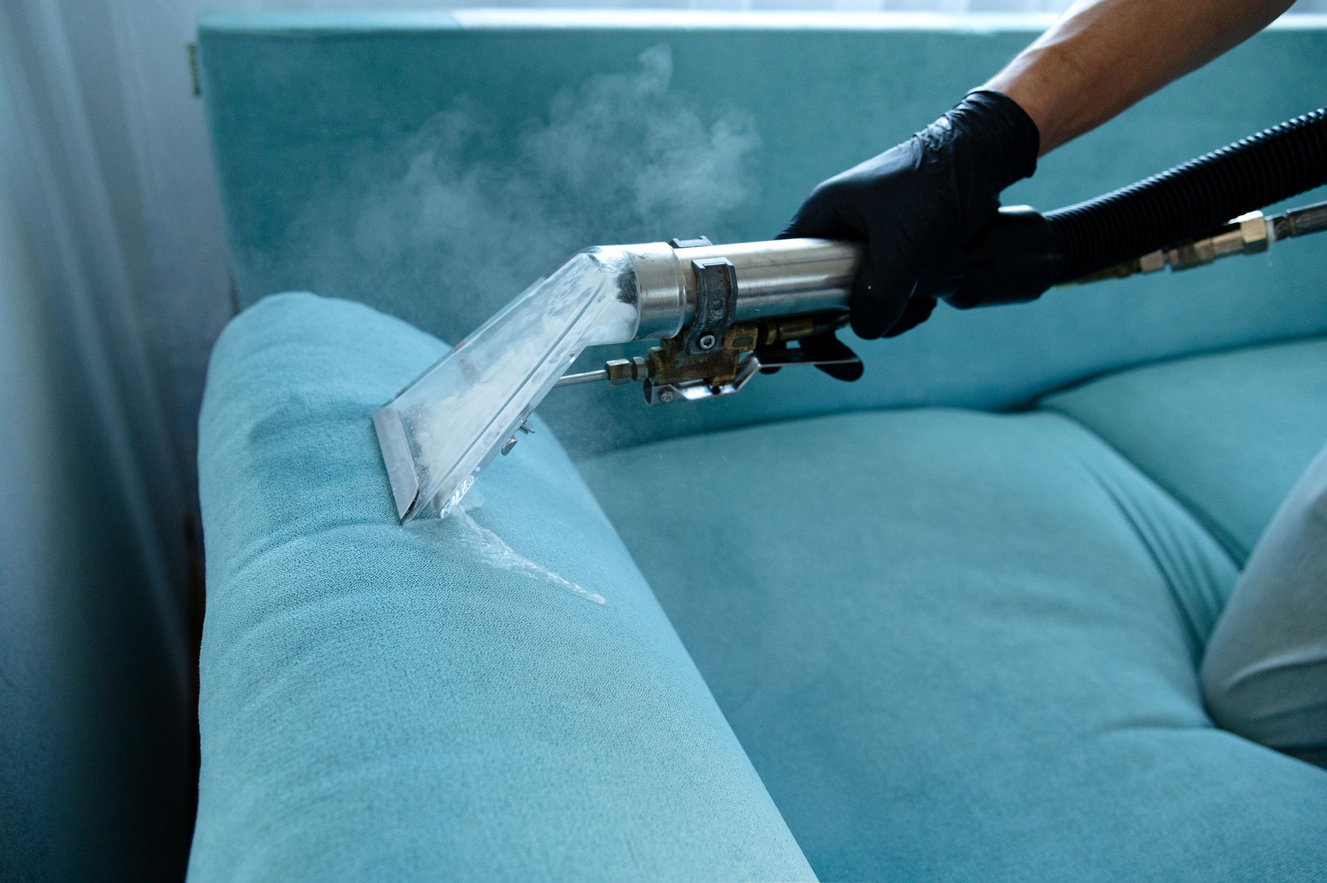 A person is cleaning a blue couch with a vacuum cleaner.