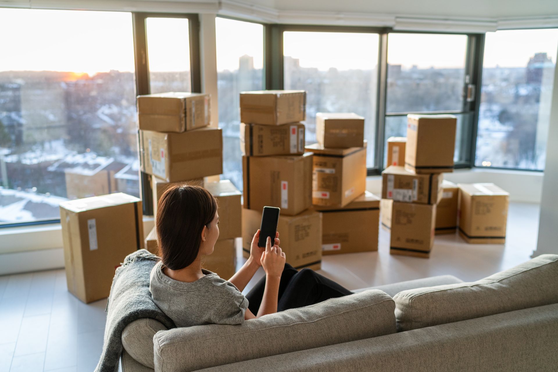 A woman is sitting on a couch in front of a pile of cardboard boxes.