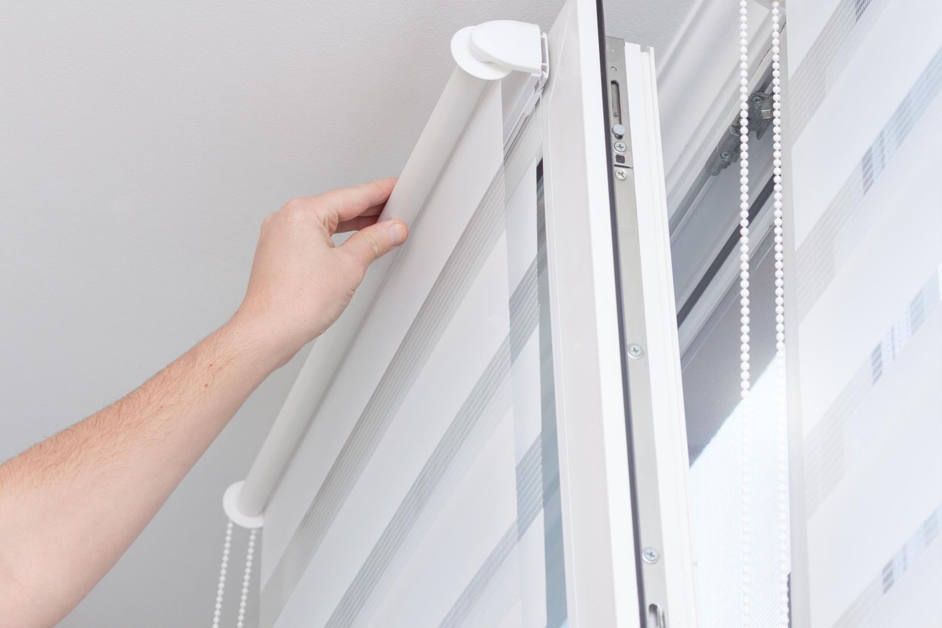 A person is adjusting a roller blind on a window.