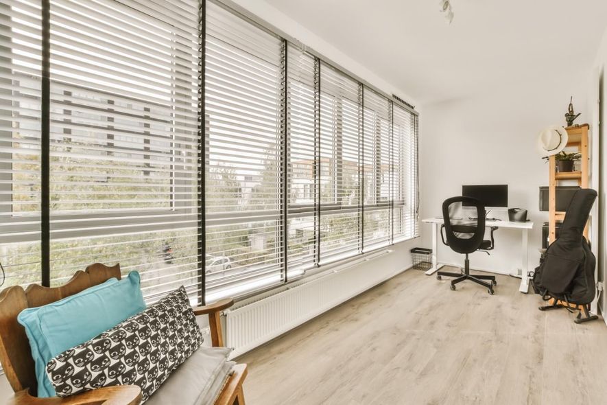 A living room with a large window, a chair, a desk and a computer.