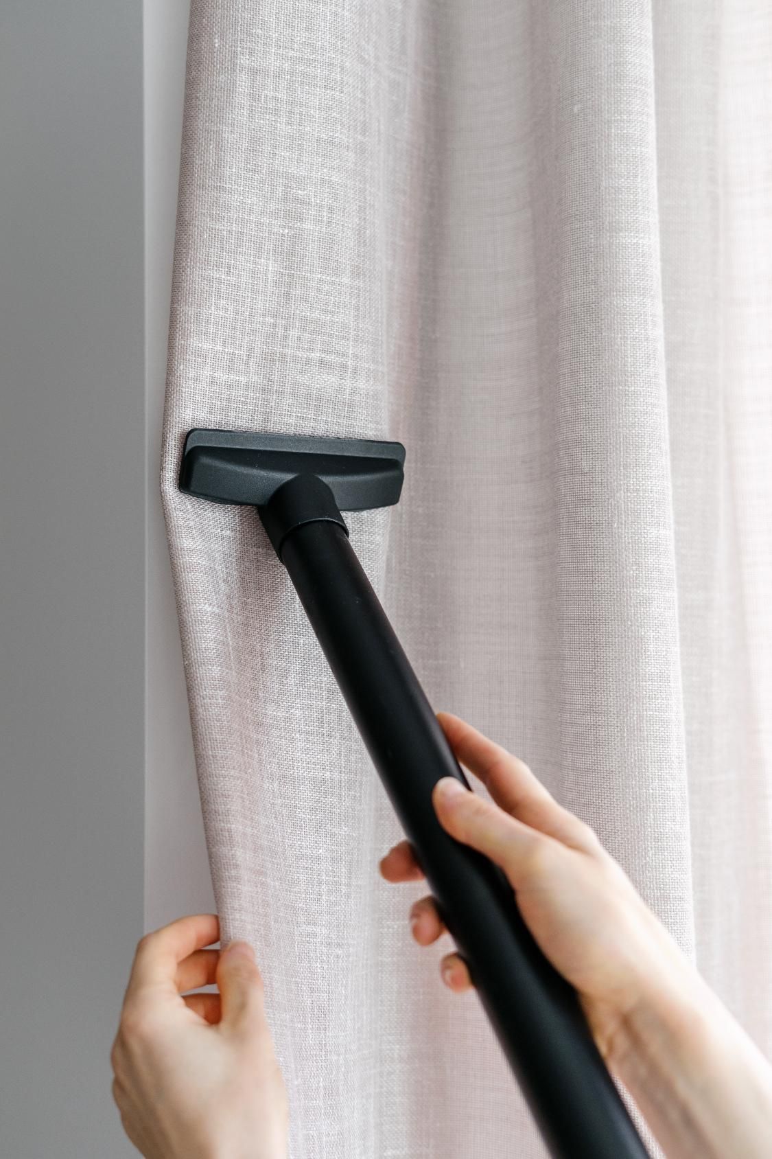 A person is cleaning a curtain with a vacuum cleaner.