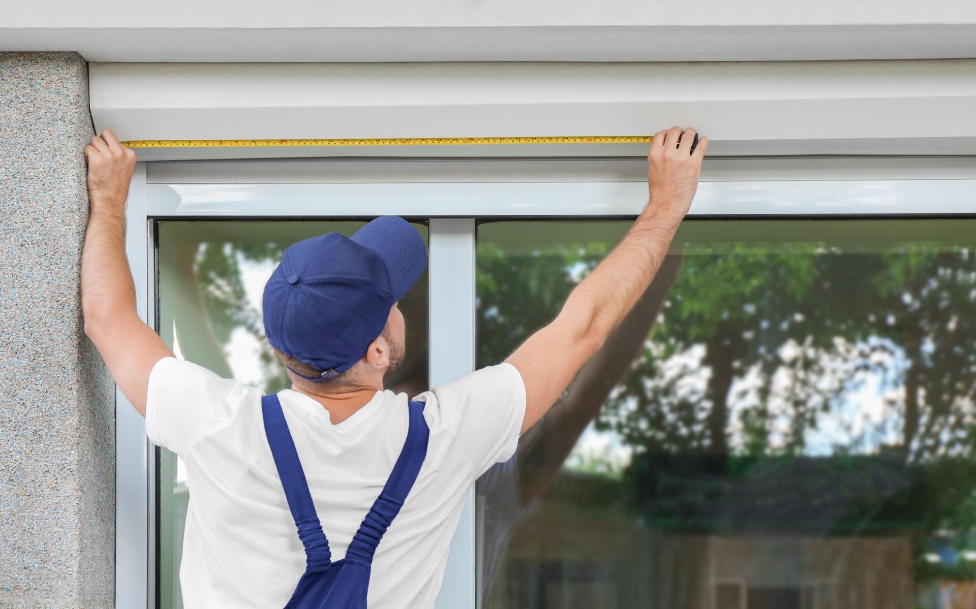 A man is measuring a window with a tape measure.