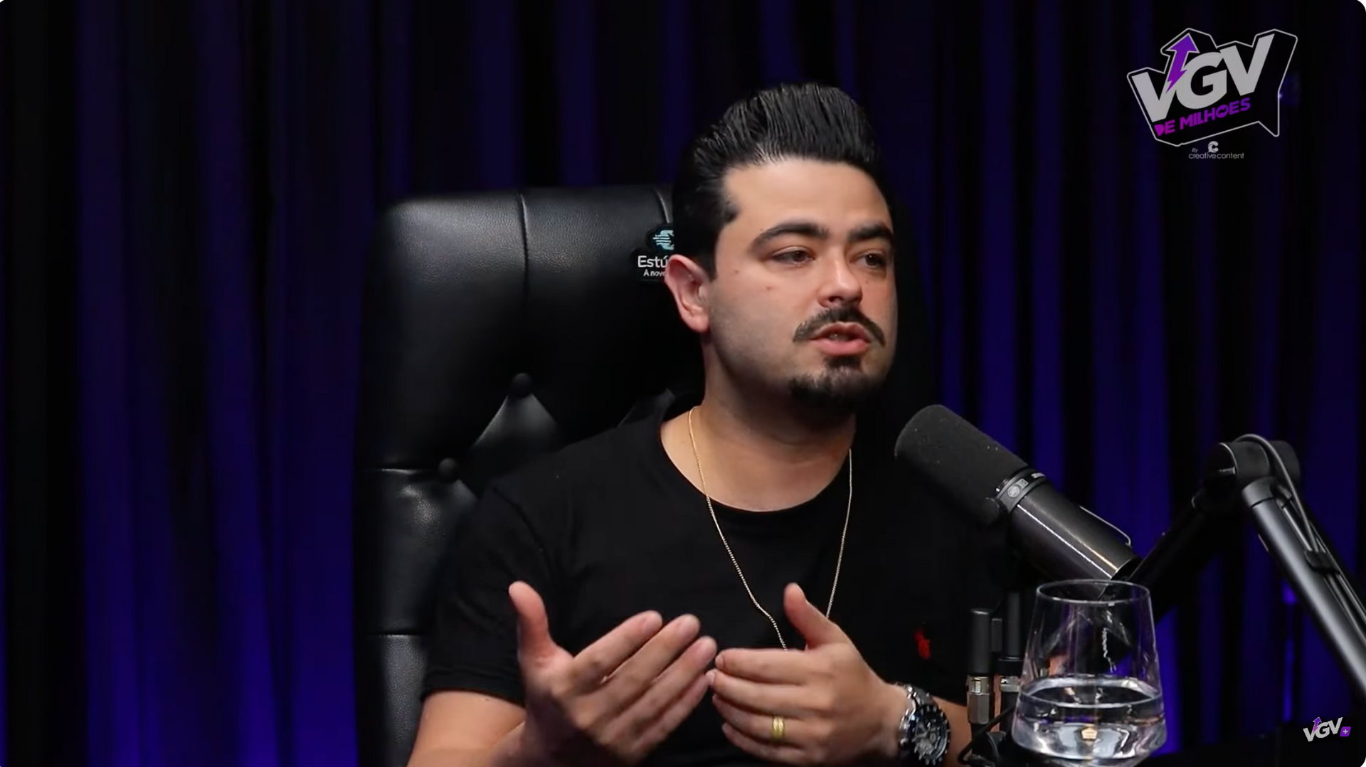 Um homem está sentado em frente a um microfone falando nele.